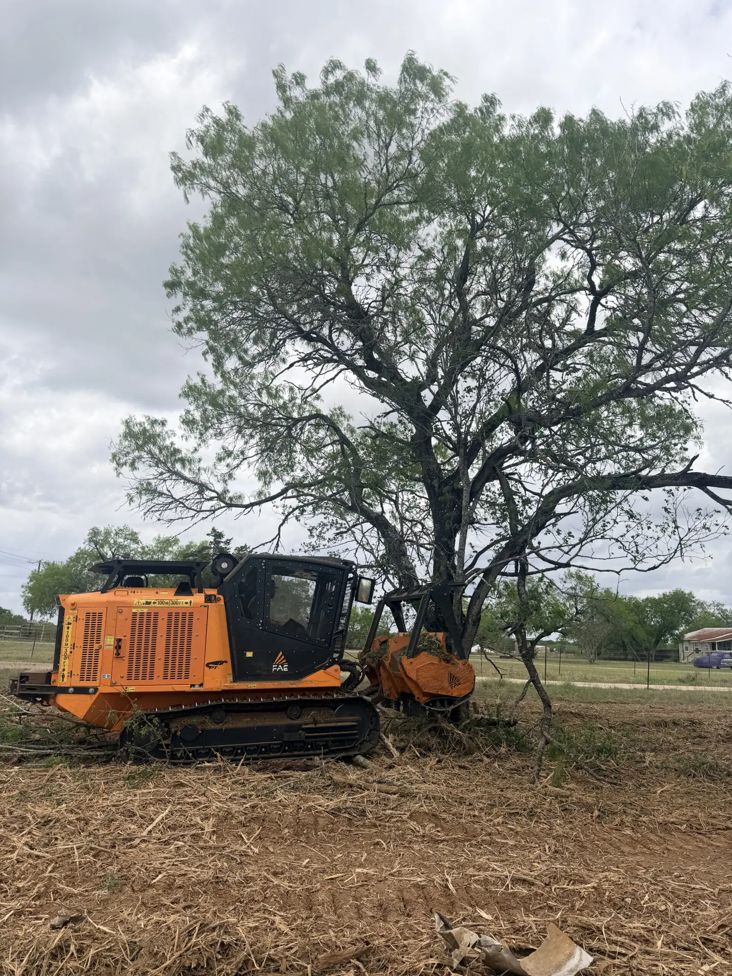 Close-up action shot of Hilliland Contracting FAE track forestry mulcher drum pressed against tree trunk and roots during residential land clearing near Seguin, TX