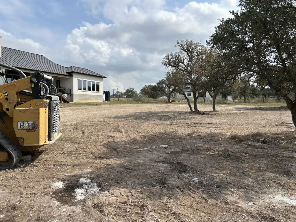 Hilliland Contracting CAT compact track loader on a cleared residential lot during land clearing and site preparation next to a modern home near Seguin, TX