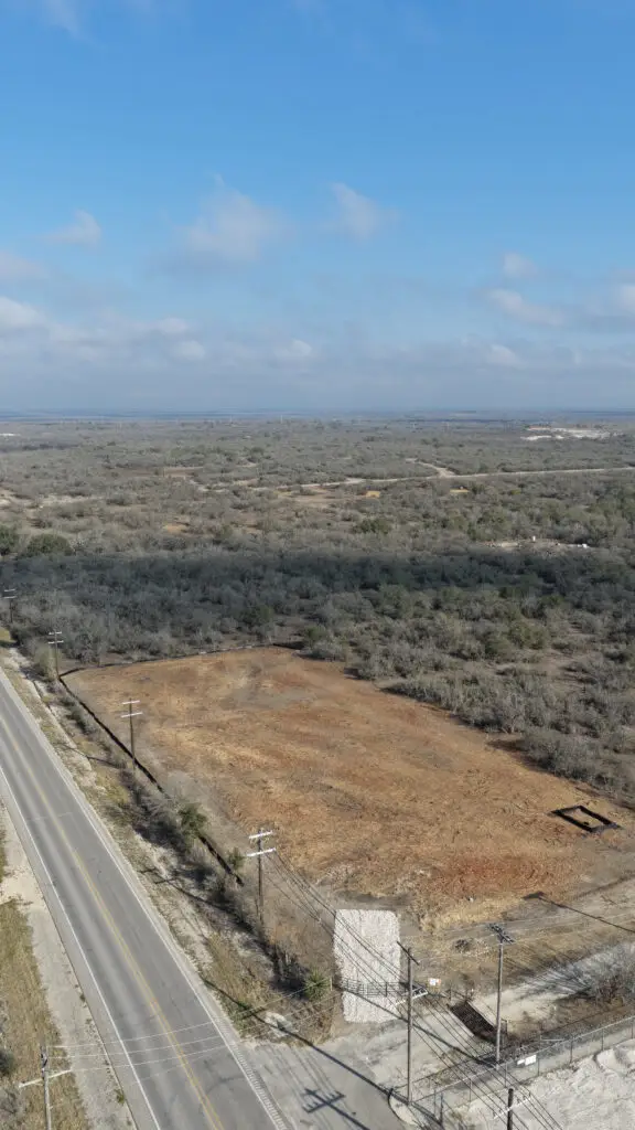 Aerial drone view of Hilliland Contracting fully cleared roadside lot with caliche surface and utility poles on a rural South Texas road near Seguin, TX